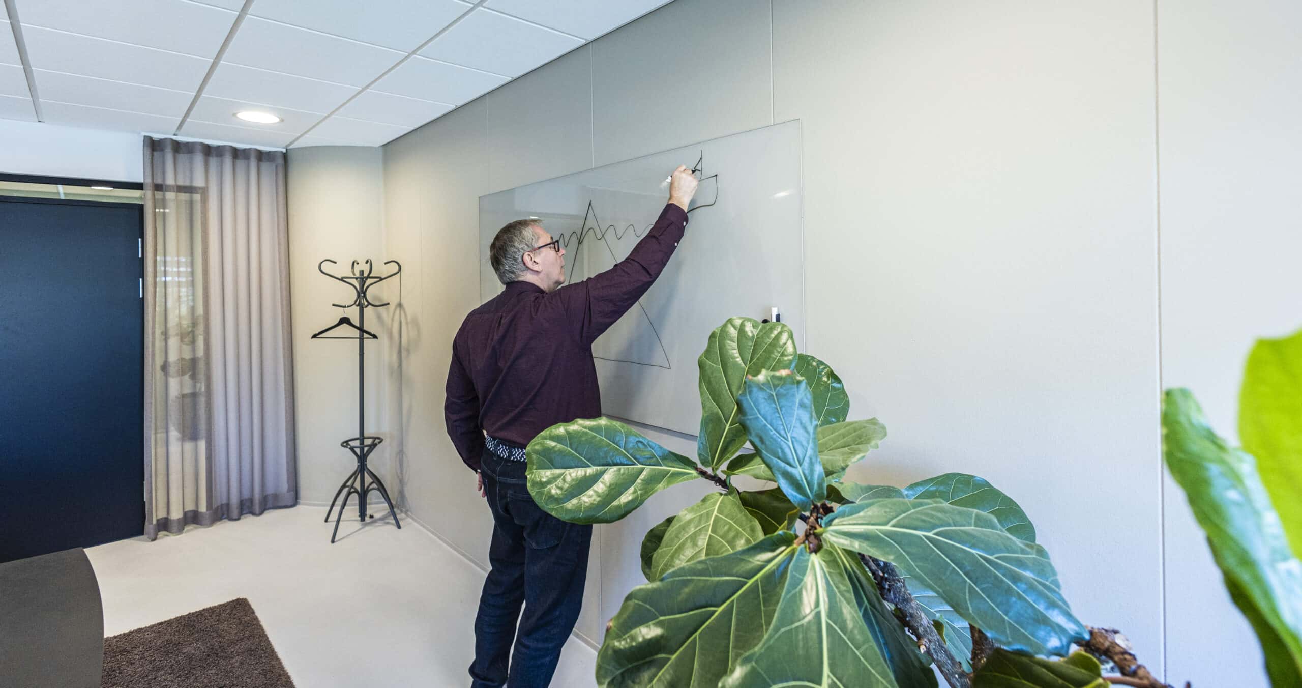 Michael Bisling tegner en isbjergsmodel på en glasskrivetavle i sin klinik.